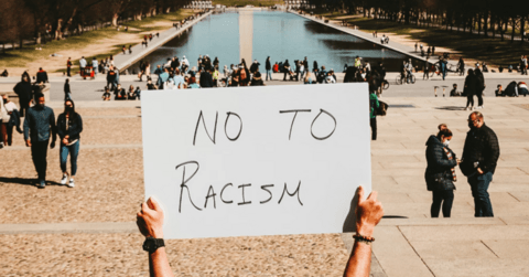 A person holding a "NO TO RACISM" sign in front of the Lincoln Memorial Reflecting Pool